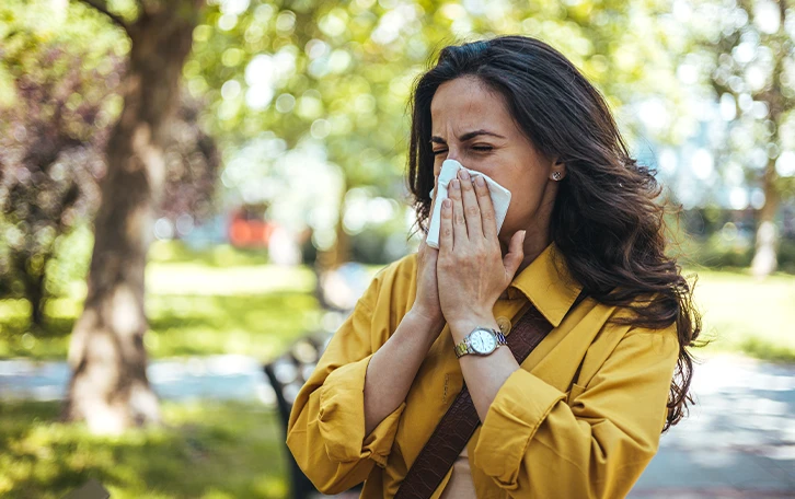 Eine weibliche Person unter Bäumen putzt sich die Nase