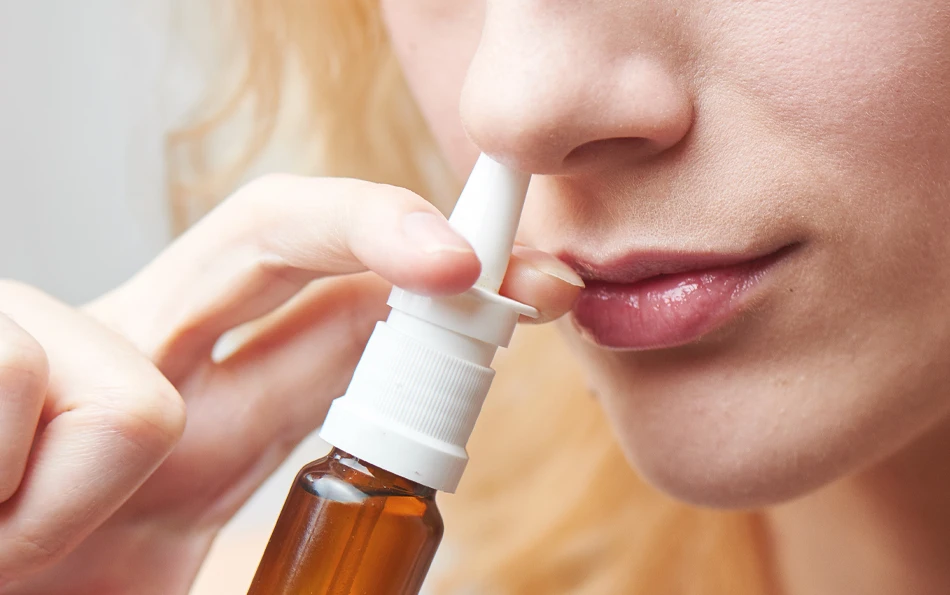 behandlung-nasenspray-bei-heuschnupfen Eine weibliche Person verabreicht sich ein Nasenspray