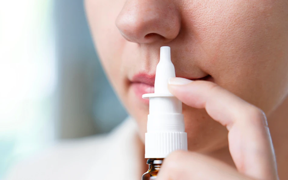Eine weibliche Person hält sich ein Nasenspray an die Nase