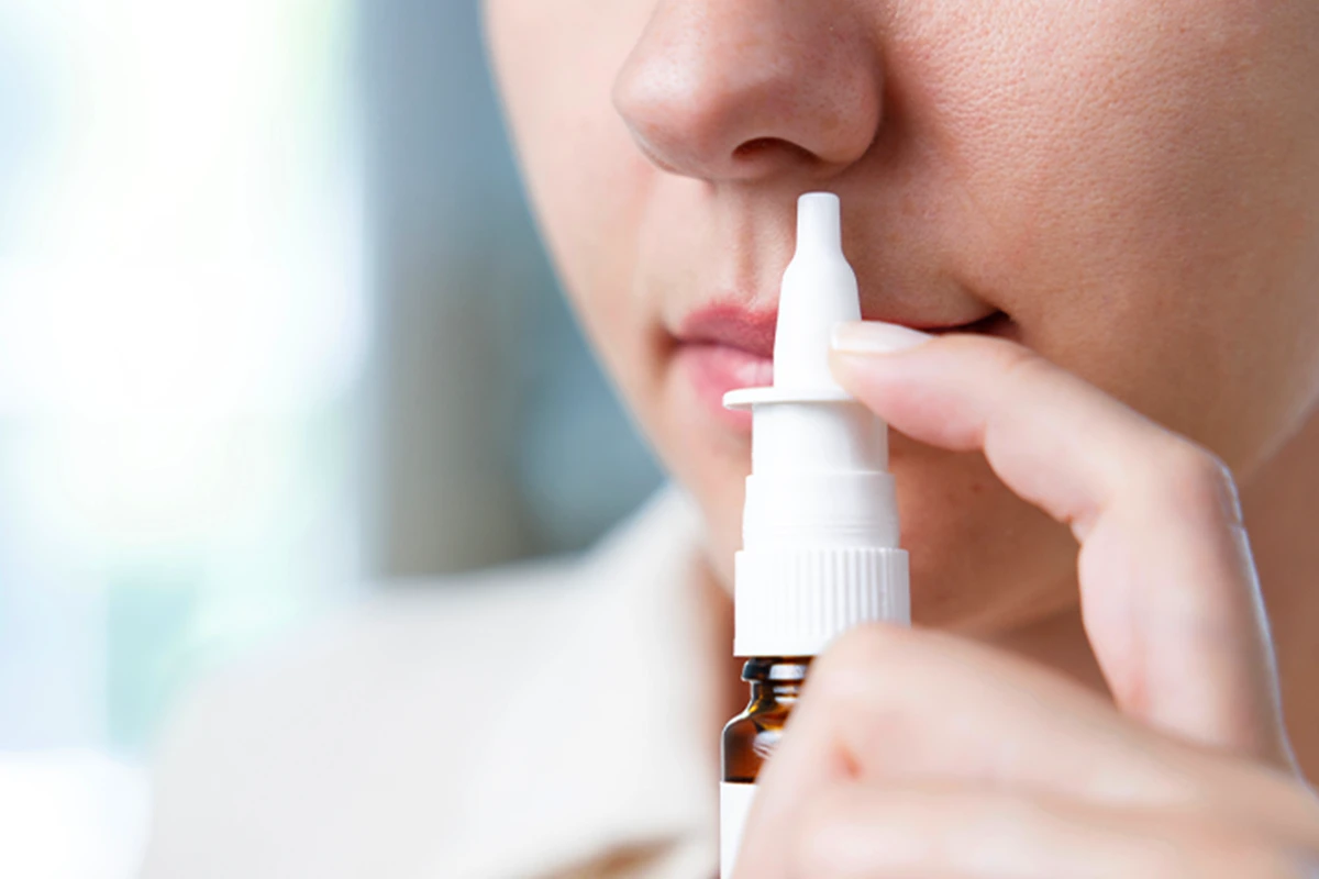 Behandlung von allergischen Schnupfen Eine weibliche Person hält sich ein Nasenspray an die Nase