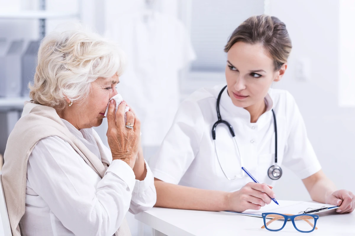 Ein weibliches medizinisches Personal sitzt mit Klemmbrett neben einer älteren weiblichen Person