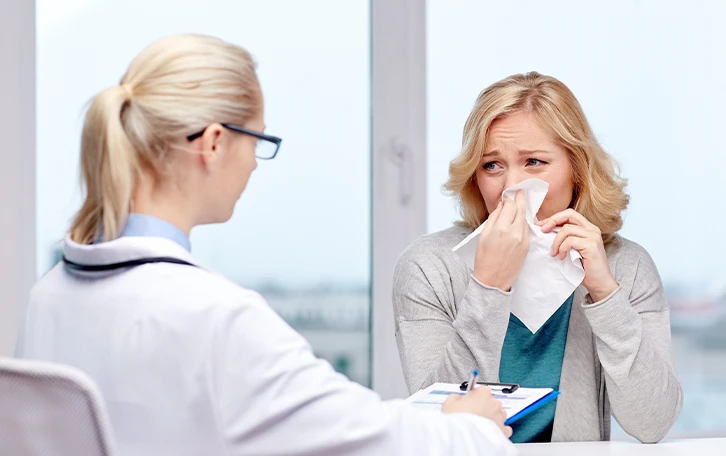 Eine weibliche Person reibt sich ein Auge mit einem Taschentuch vor einer weiblichen ärztlichen Kraft