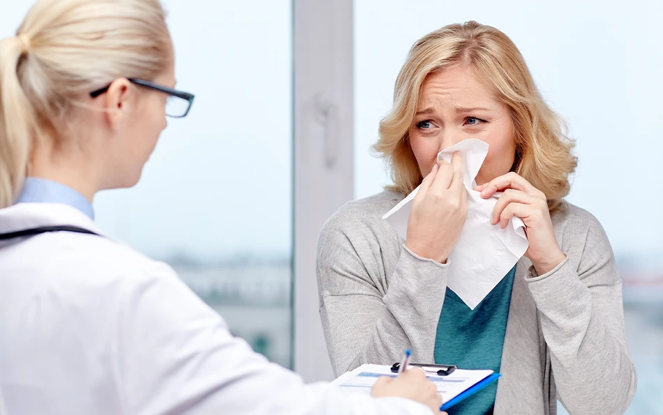 Eine weibliche Person reibt sich ein Auge mit einem Taschentuch vor einer weiblichen ärztlichen Kraft