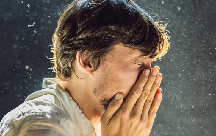 Eine männliche Person beim nießen mit vielen Partikeln um sich herum