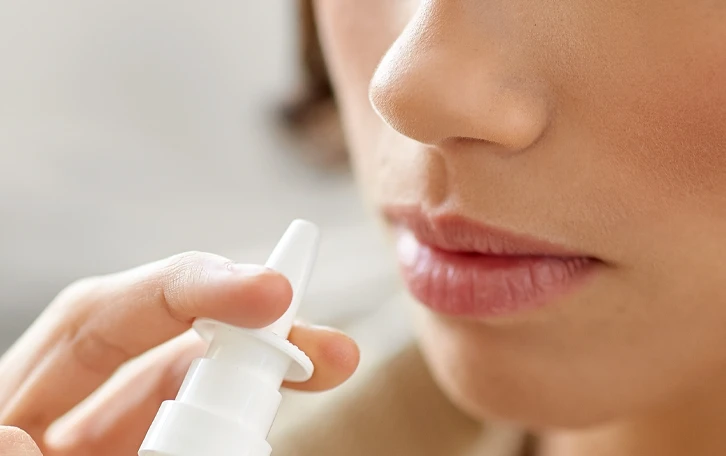 Eine weibliche Person hält sich ein Nasenspray an die Nase