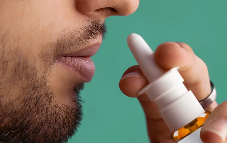 Eine männliche Person hält sich ein Nasenspray an die Nase