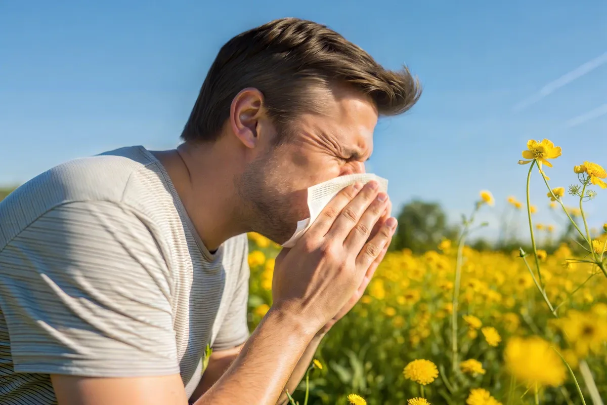 Eine männliche Person putzt sich auf einer blühenden Wiese die Nase