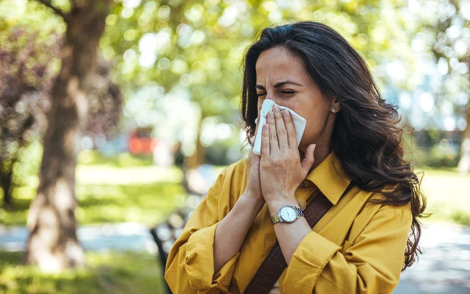 Eine weibliche Person unter Bäumen putzt sich die Nase