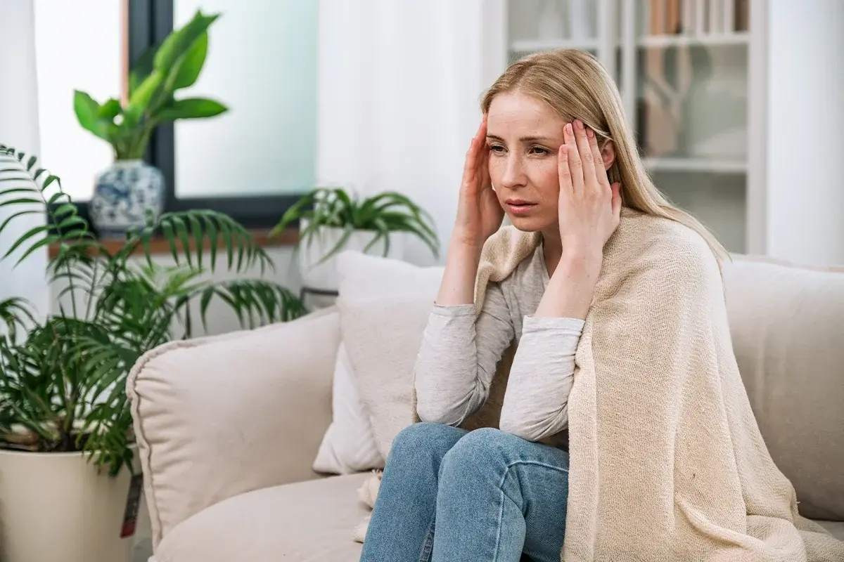 Heuschnupfen Weitere Symptome Eine weibliche Person auf einer Couch sitzend hält sich die Schläfen