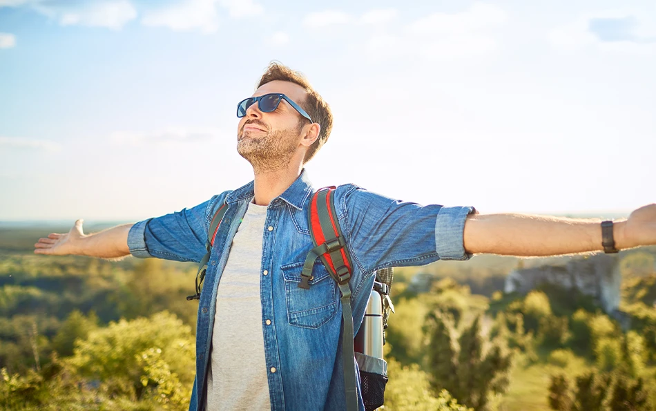 Eine männliche Person mit ausgebreiteten Armen mit Sonnenbrille auf und Rucksack auf