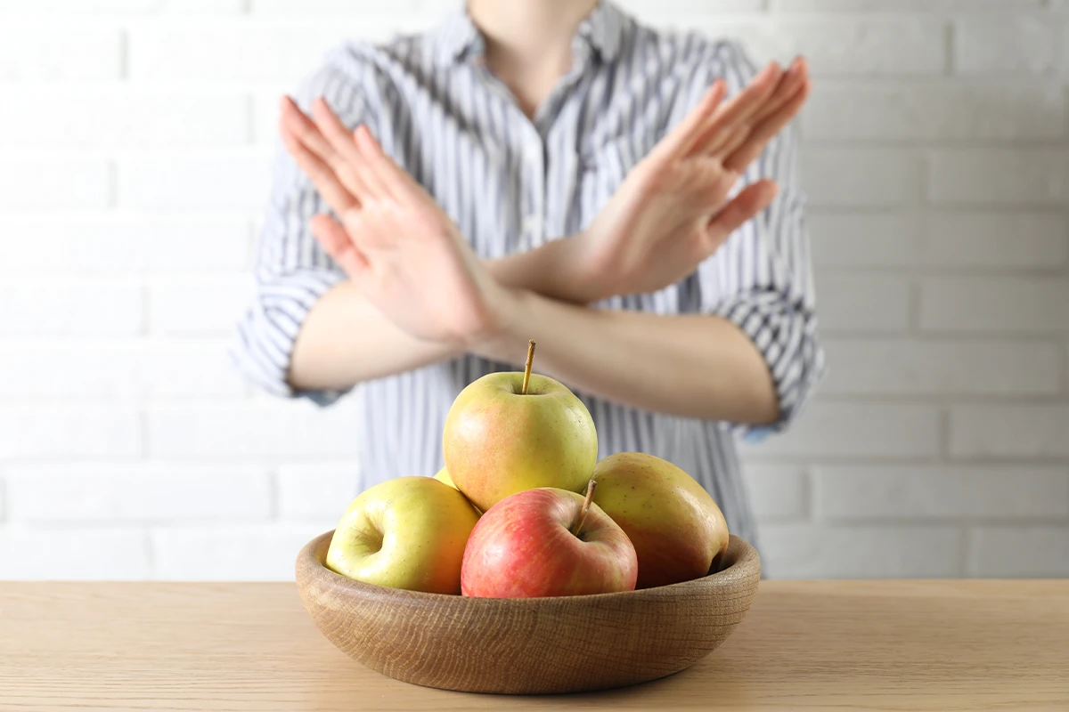 Kreuzallergien bei Haselallergikern Risiken Eine Person mit verschränkten Armen vor einer Schüssel voll mit Äpfeln