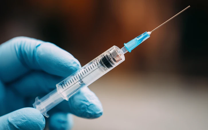 Eine Hand im Latexhandschuh hält eine Spritze