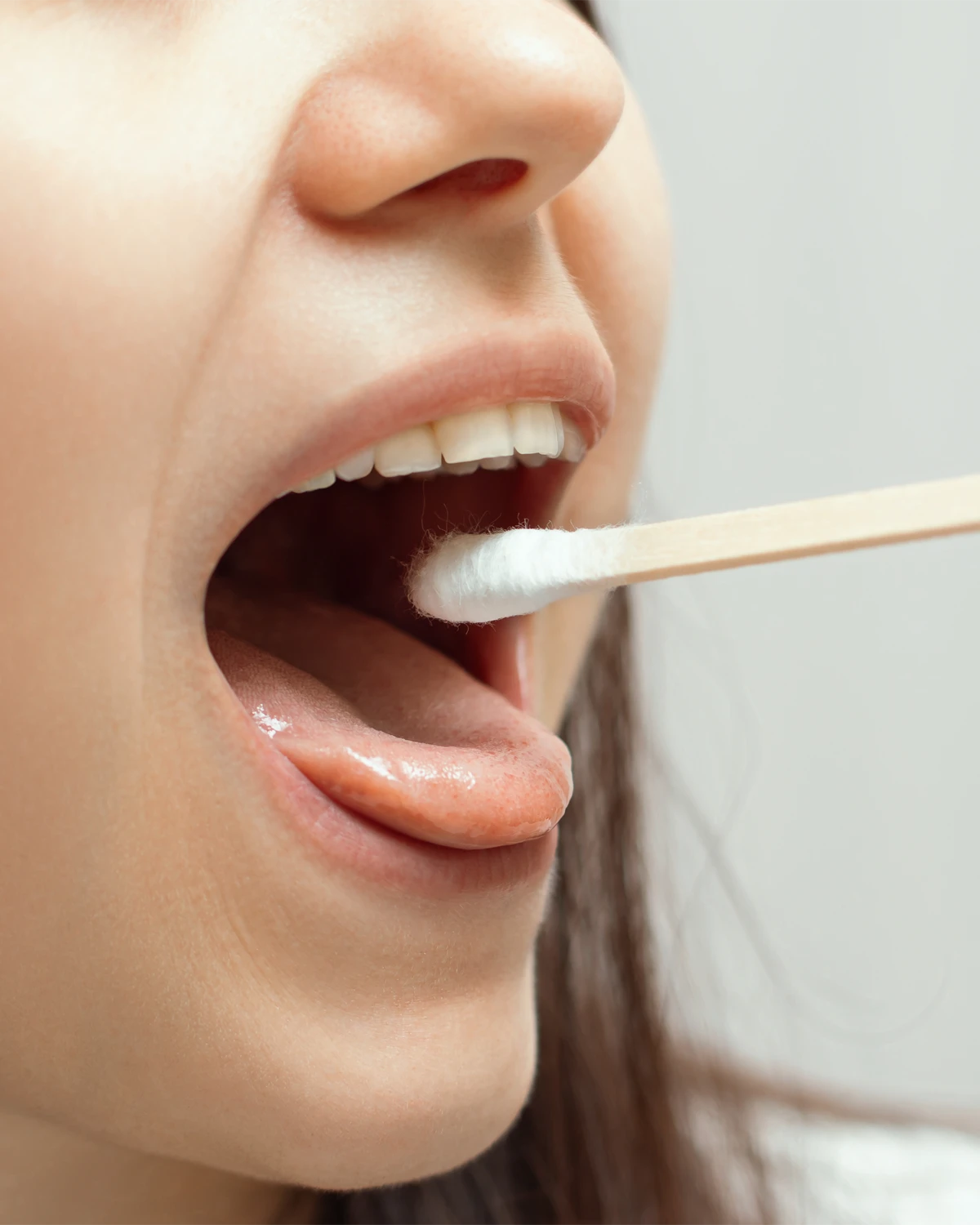 Eine weibliche Person hat den Mund weit geöffnet und ein Wattestäbchen ist über der Zunge