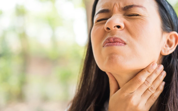 Eine weibliche Person hält sich mit geschlossenen Augen den Hals