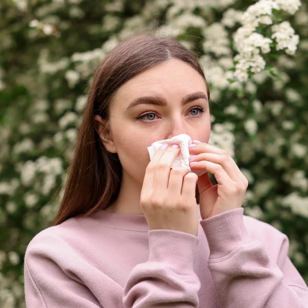 Typische Beschwerden der Haselallergie Eine weibliche Person in der Natur putzt sich die Nase