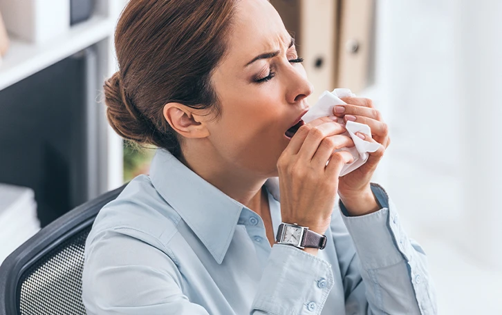Eine weibliche Person mit Taschentuch vorm Gesicht beim Nießen