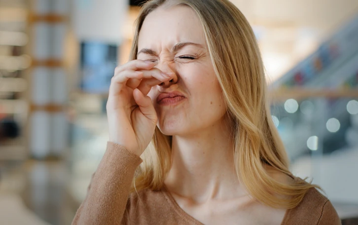 Eine weibliche Person mit geschlossenen Augen und verzogenem Gesicht reibt sich die Nase