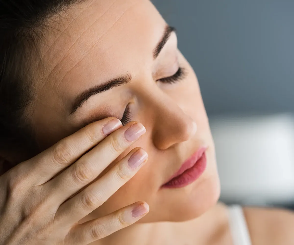 Typische Symptome der Birkenpollenallergie Eine weibliche Person mit geschlossenen Augen reibt sein das rechte Auge