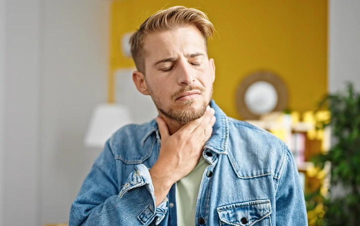 Eine männliche Person greift sich mit geschlossenen Augen an den Hals