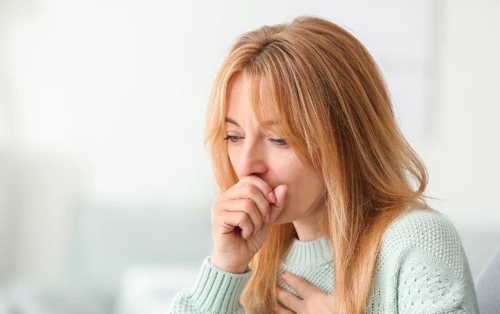 Eine weibliche Person beim Husten mit Hand vorm Mund und auf dem Brustkorb