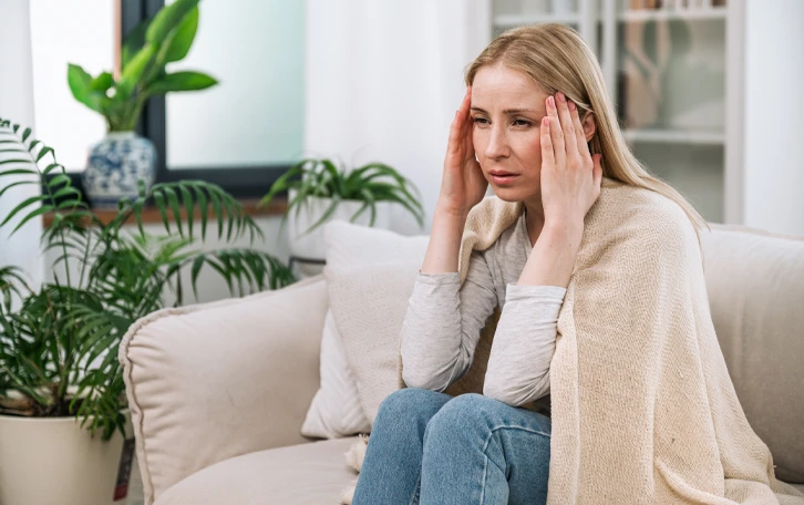 Eine weibliche Person auf einer Couch sitzend hält sich die Schläfen