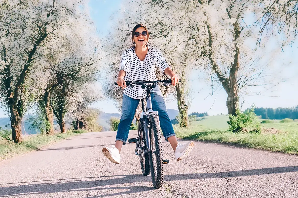Was ist Heuschnupfen Hintergruende Eine weibliche Person unter den Bäumen einer Alle auf einem Fahrrad fahrend mit den Beinen von den Pedalen weg gestreckt